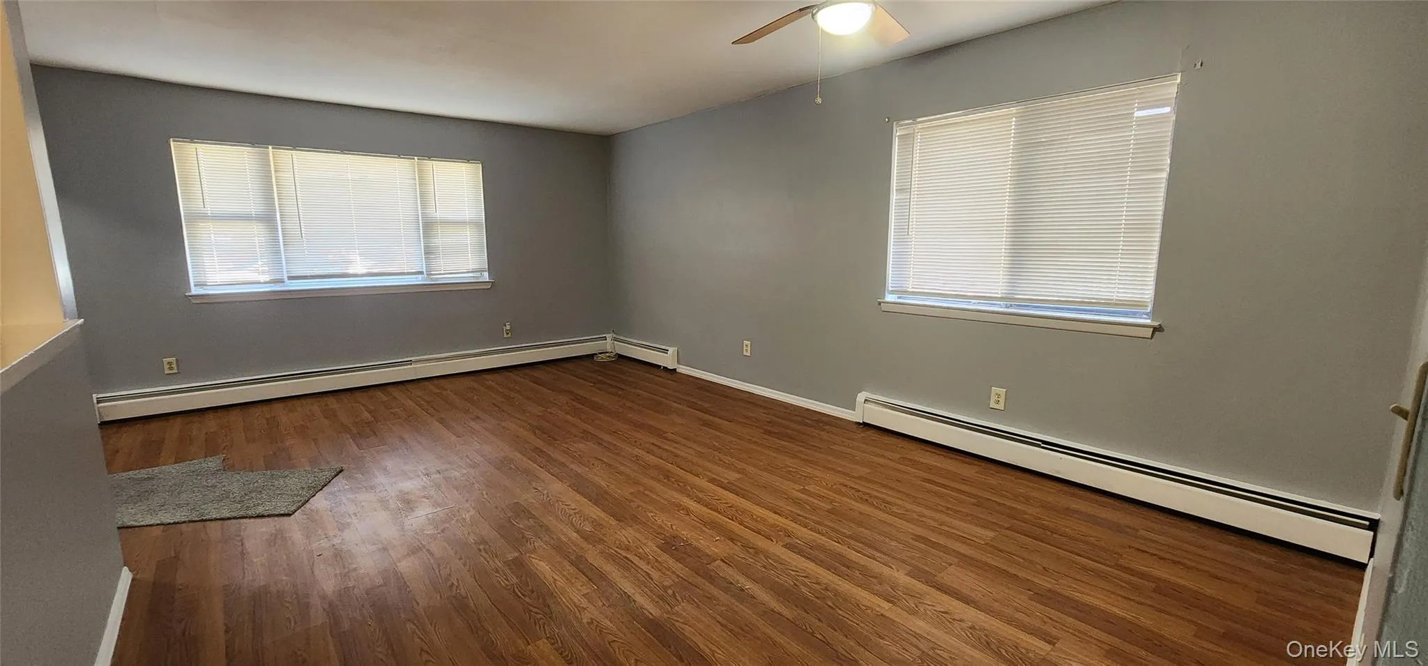 Spare room featuring a baseboard heating unit, dark wood-style floors, and a ceiling fan Spare room featuring a baseboard heating unit, dark wood-style floors, and a ceiling fan