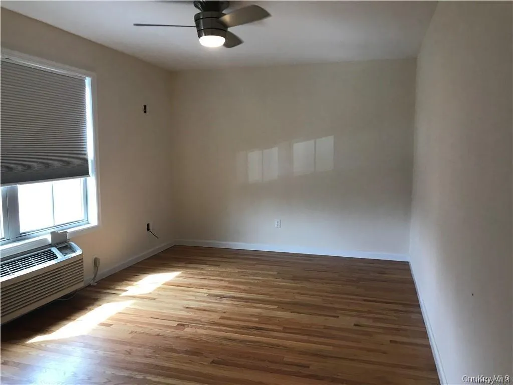 Empty room featuring light wood-type flooring, ceiling fan, and cooling unit Empty room featuring light wood-type flooring, ceiling fan, and cooling unit