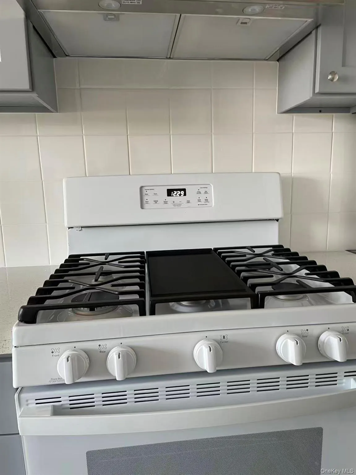 Kitchen view of extractor fan, white gas range, backsplash, and gray cabinetry Kitchen view of extractor fan, white gas range, backsplash, and gray cabinetry