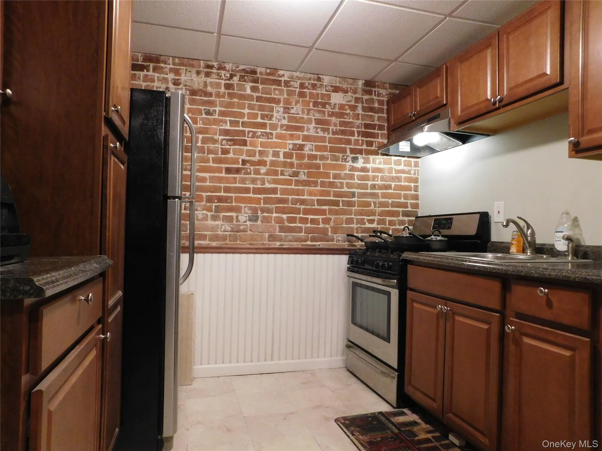 Kitchen with brick wall, wainscoting, stainless steel appliances, a drop ceiling, and under cabinet range hood Kitchen with brick wall, wainscoting, stainless steel appliances, a drop ceiling, and under cabinet range hood