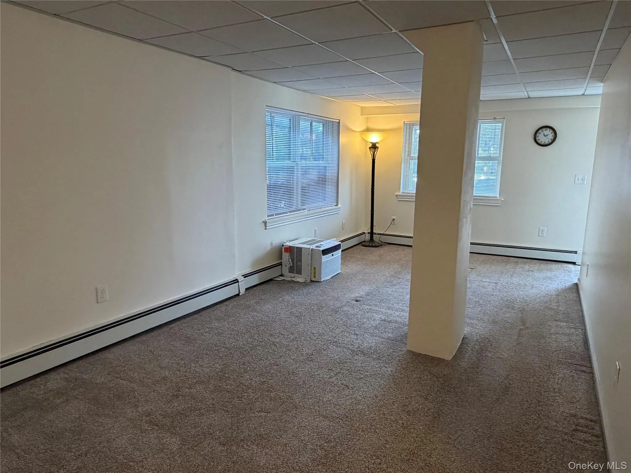 Below grade area featuring a baseboard heating unit, light colored carpet, and a paneled ceiling Below grade area featuring a baseboard heating unit, light colored carpet, and a paneled ceiling