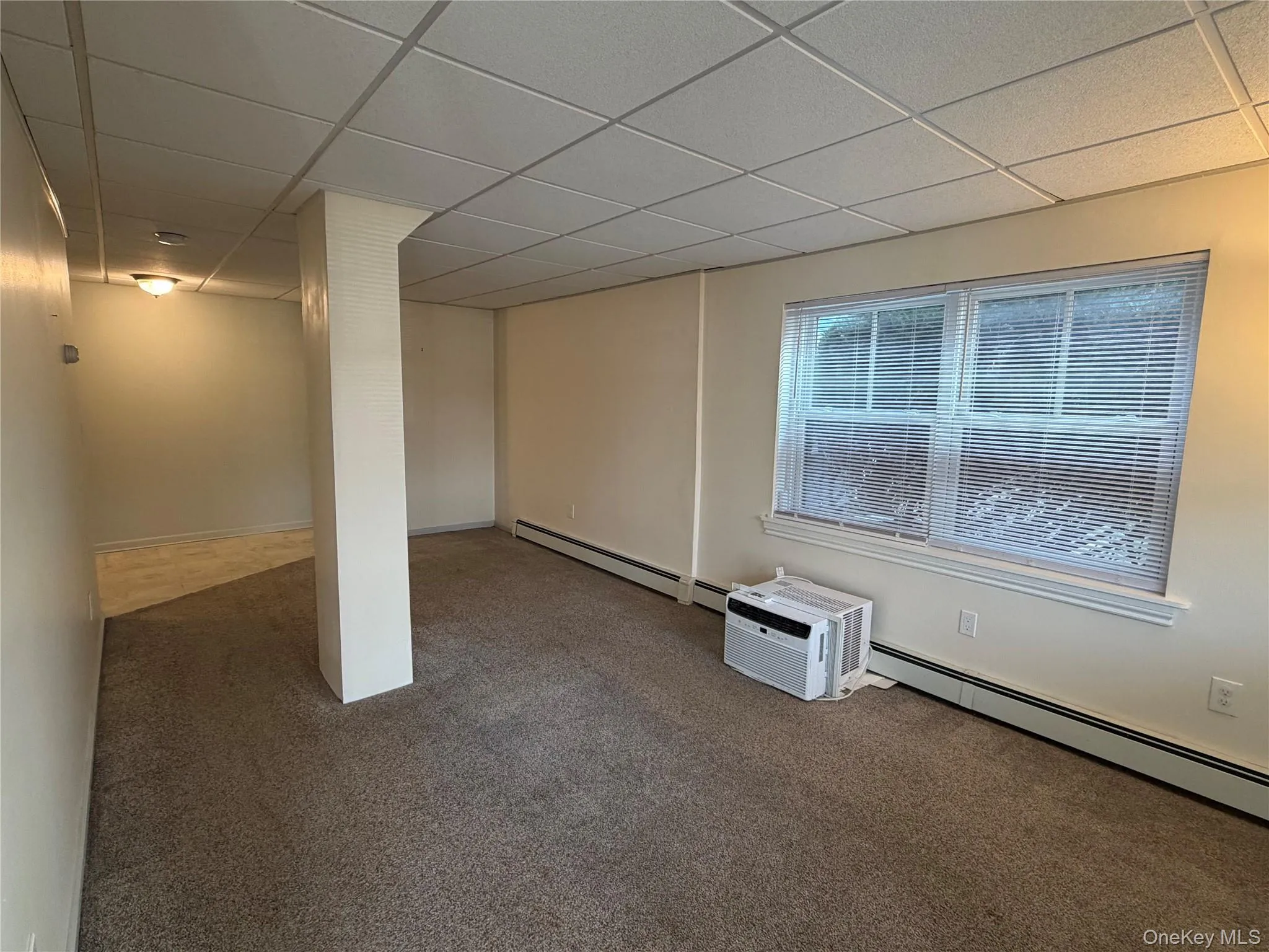 Below grade area featuring a paneled ceiling, carpet, and a baseboard heating unit Below grade area featuring a paneled ceiling, carpet, and a baseboard heating unit