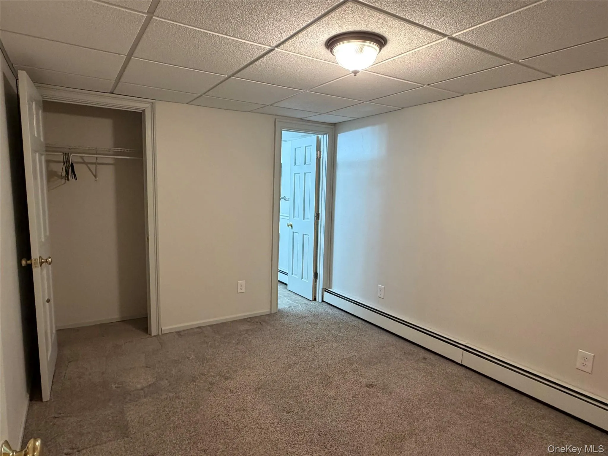 Unfurnished bedroom featuring a baseboard radiator, a paneled ceiling, light carpet, and a closet Unfurnished bedroom featuring a baseboard radiator, a paneled ceiling, light carpet, and a closet