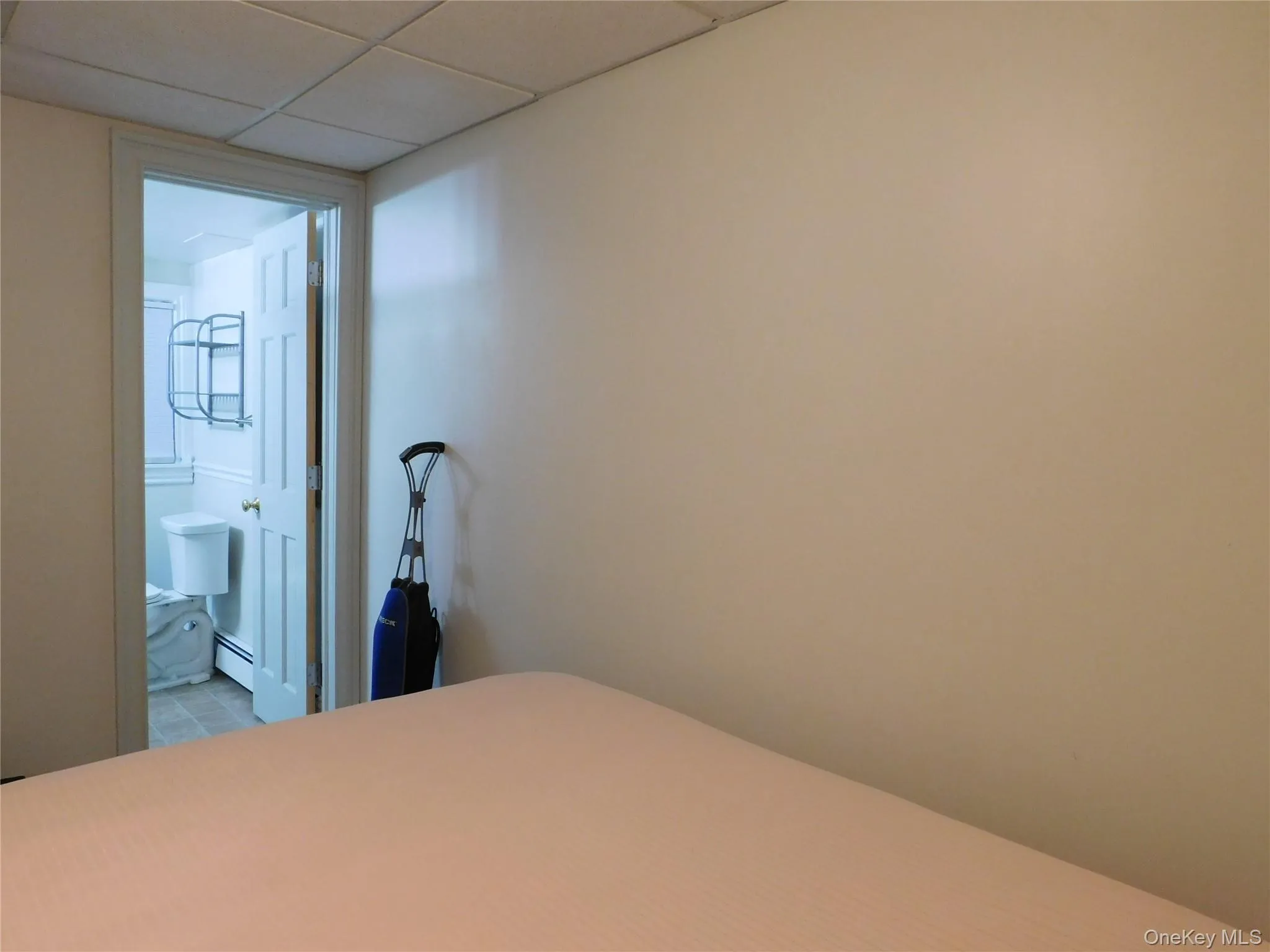 Bedroom featuring a paneled ceiling, connected bathroom, and a baseboard heating unit Bedroom featuring a paneled ceiling, connected bathroom, and a baseboard heating unit