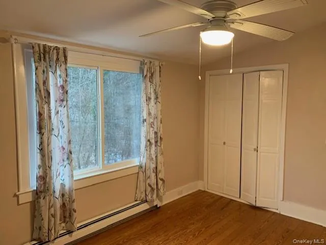 Unfurnished bedroom featuring multiple windows, baseboard heating, ceiling fan, and wood finished floors Unfurnished bedroom featuring multiple windows, baseboard heating, ceiling fan, and wood finished floors