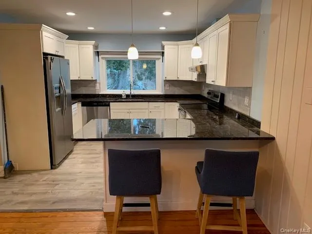 Kitchen featuring appliances with stainless steel finishes, decorative light fixtures, a breakfast bar, a peninsula, and white cabinets Kitchen featuring appliances with stainless steel finishes, decorative light fixtures, a breakfast bar, a peninsula, and white cabinets