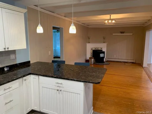 Kitchen featuring open floor plan, a peninsula, light wood finished floors, white cabinetry, and dark stone counters Kitchen featuring open floor plan, a peninsula, light wood finished floors, white cabinetry, and dark stone counters