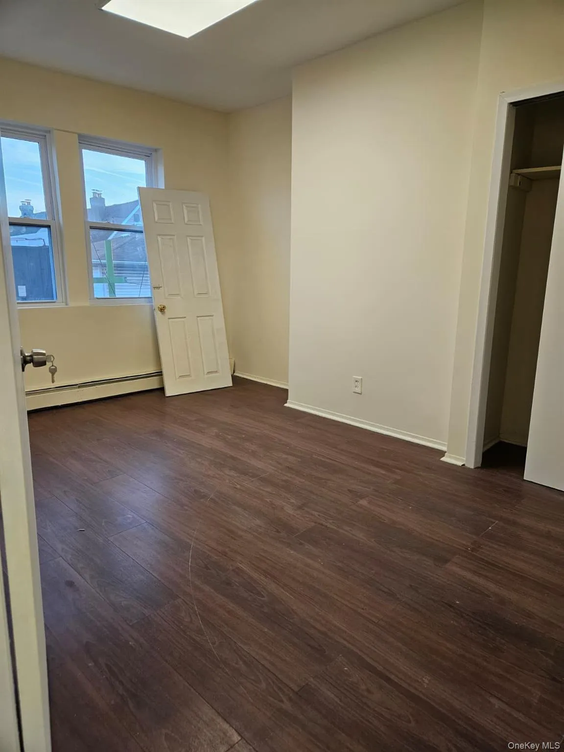 Unfurnished bedroom featuring dark wood-style floors, a baseboard heating unit, a skylight, and a closet Unfurnished bedroom featuring dark wood-style floors, a baseboard heating unit, a skylight, and a closet