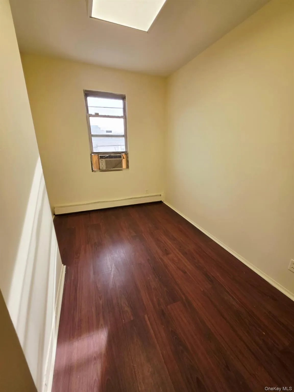 Empty room with dark wood-style floors, a baseboard heating unit, and cooling unit Empty room with dark wood-style floors, a baseboard heating unit, and cooling unit