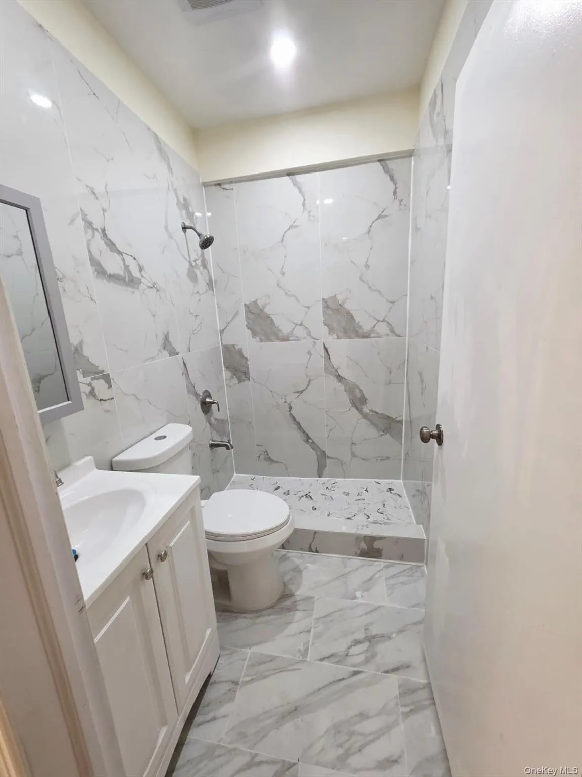 Bathroom with a marble finish shower, vanity, light marble finish floors, and tile walls Bathroom with a marble finish shower, vanity, light marble finish floors, and tile walls