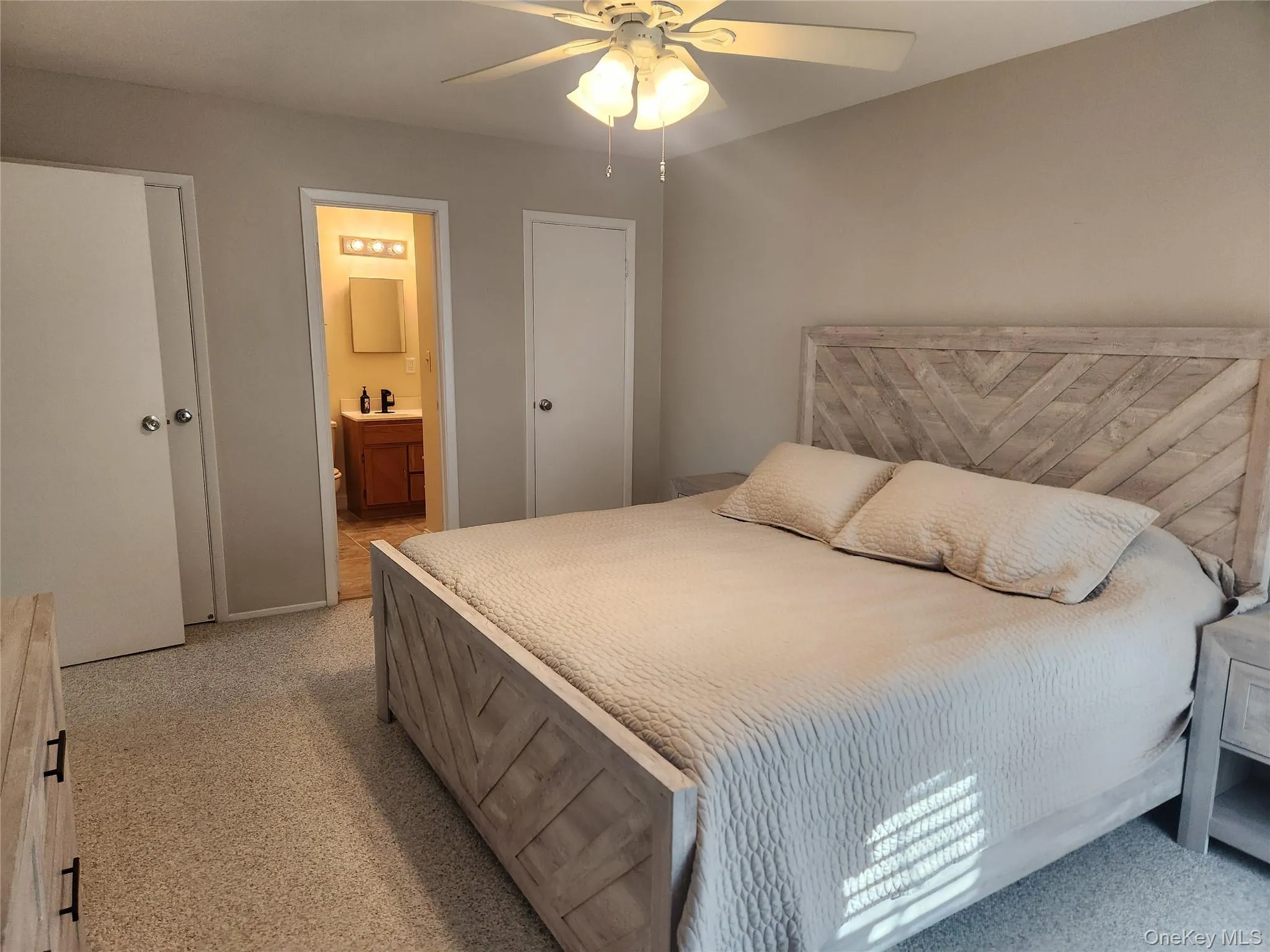 Bedroom with ensuite bathroom, ceiling fan, and light colored carpet Bedroom with ensuite bathroom, ceiling fan, and light colored carpet