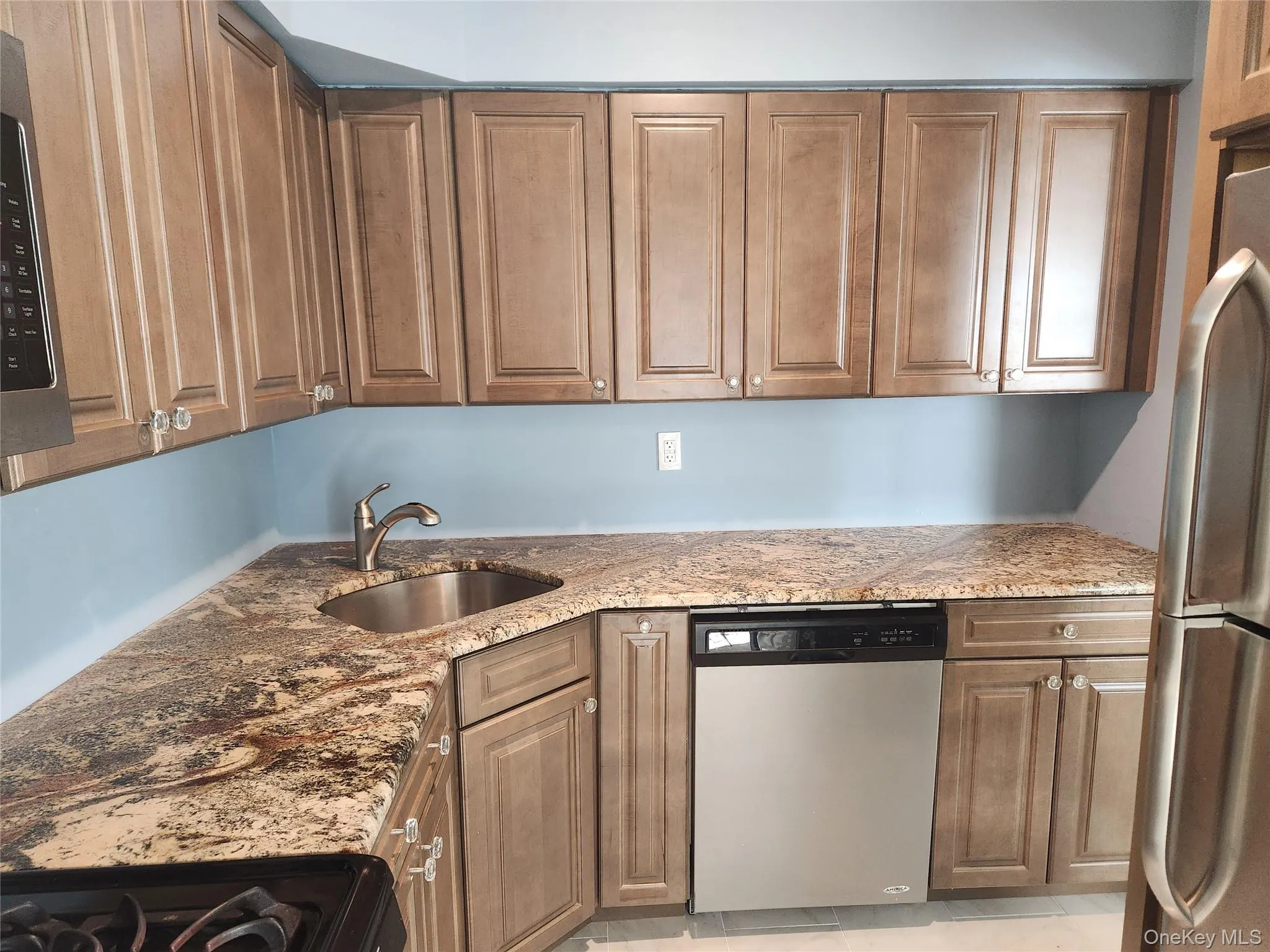 Kitchen featuring appliances with stainless steel finishes, light stone countertops, and brown cabinetry Kitchen featuring appliances with stainless steel finishes, light stone countertops, and brown cabinetry