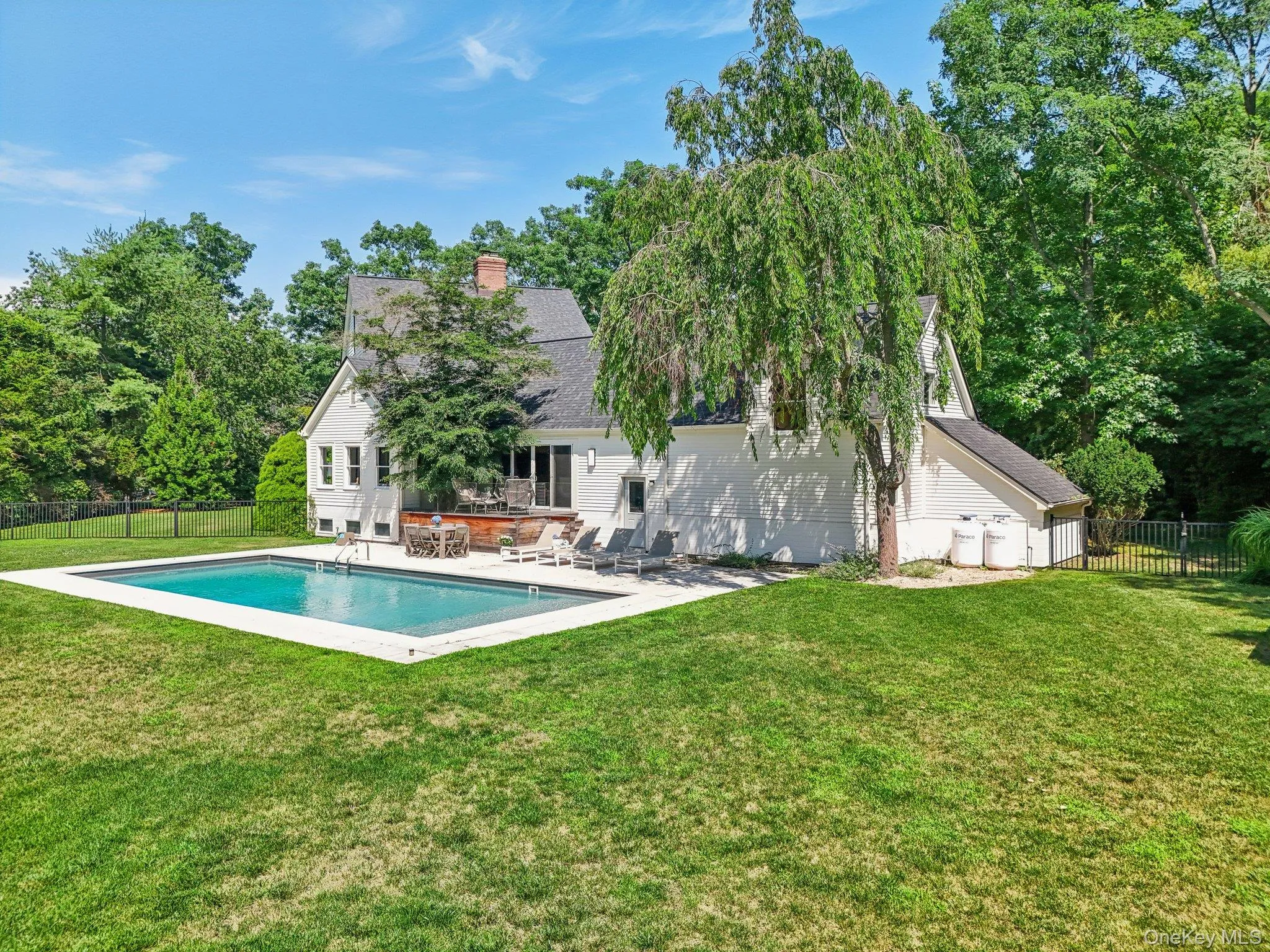 Rear view of house with a fenced backyard, a patio area, a chimney, roof with shingles, and view of wooded area Rear view of house with a fenced backyard, a patio area, a chimney, roof with shingles, and view of wooded area