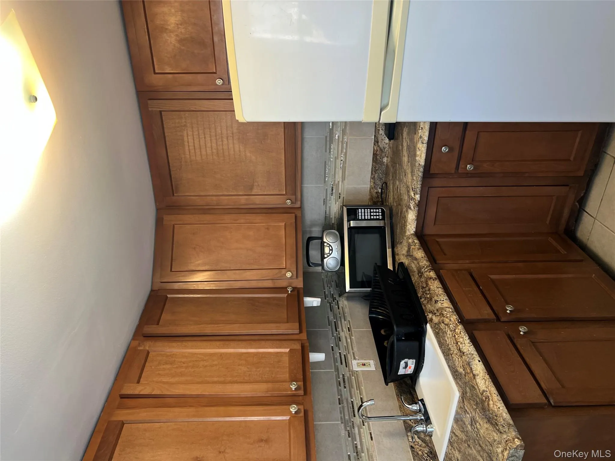 Kitchen with fridge, black microwave, brown cabinets, and tasteful backsplash Kitchen with fridge, black microwave, brown cabinets, and tasteful backsplash