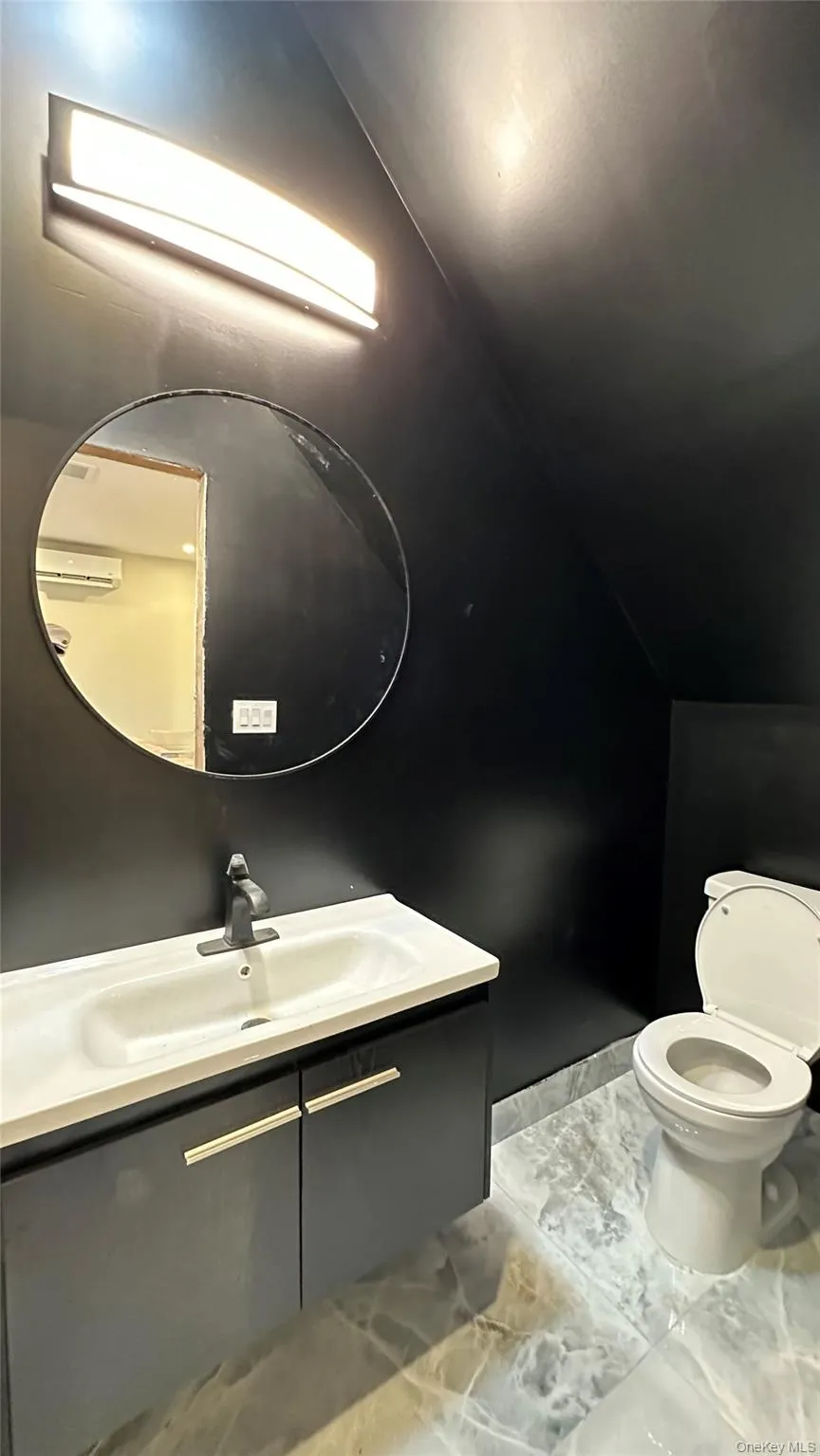 Bathroom featuring lofted ceiling, vanity, and light marble finish flooring Bathroom featuring lofted ceiling, vanity, and light marble finish flooring
