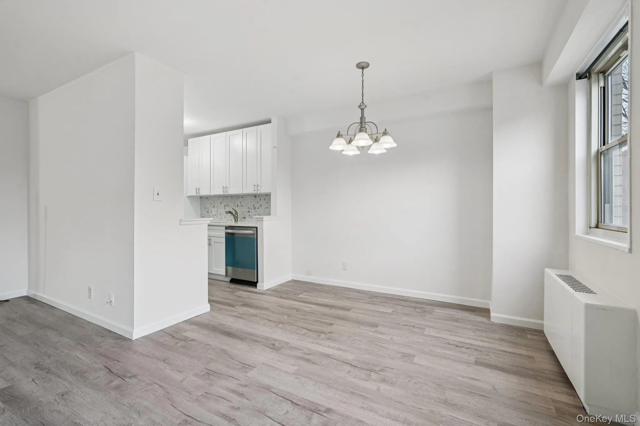 Unfurnished living room with radiator heating unit, a chandelier, and light wood-style floors Unfurnished living room with radiator heating unit, a chandelier, and light wood-style floors