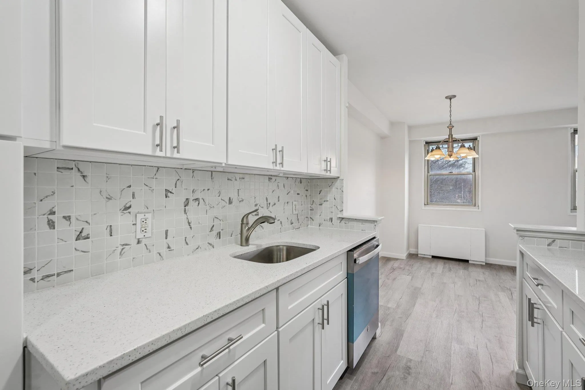 Kitchen with white cabinets, light stone counters, backsplash, light wood-type flooring, and decorative light fixtures Kitchen with white cabinets, light stone counters, backsplash, light wood-type flooring, and decorative light fixtures