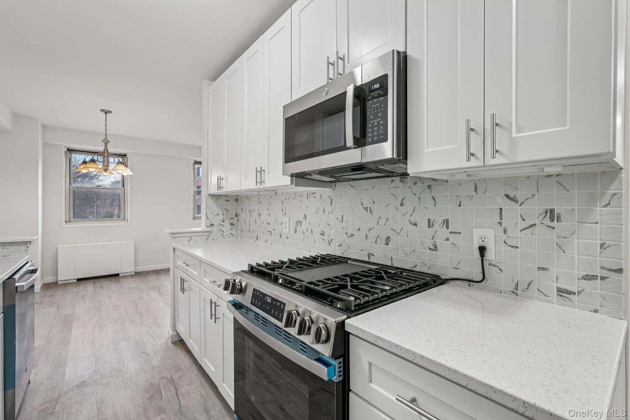 Kitchen with stainless steel appliances, pendant lighting, white cabinets, light wood-style floors, and light stone counters Kitchen with stainless steel appliances, pendant lighting, white cabinets, light wood-style floors, and light stone counters
