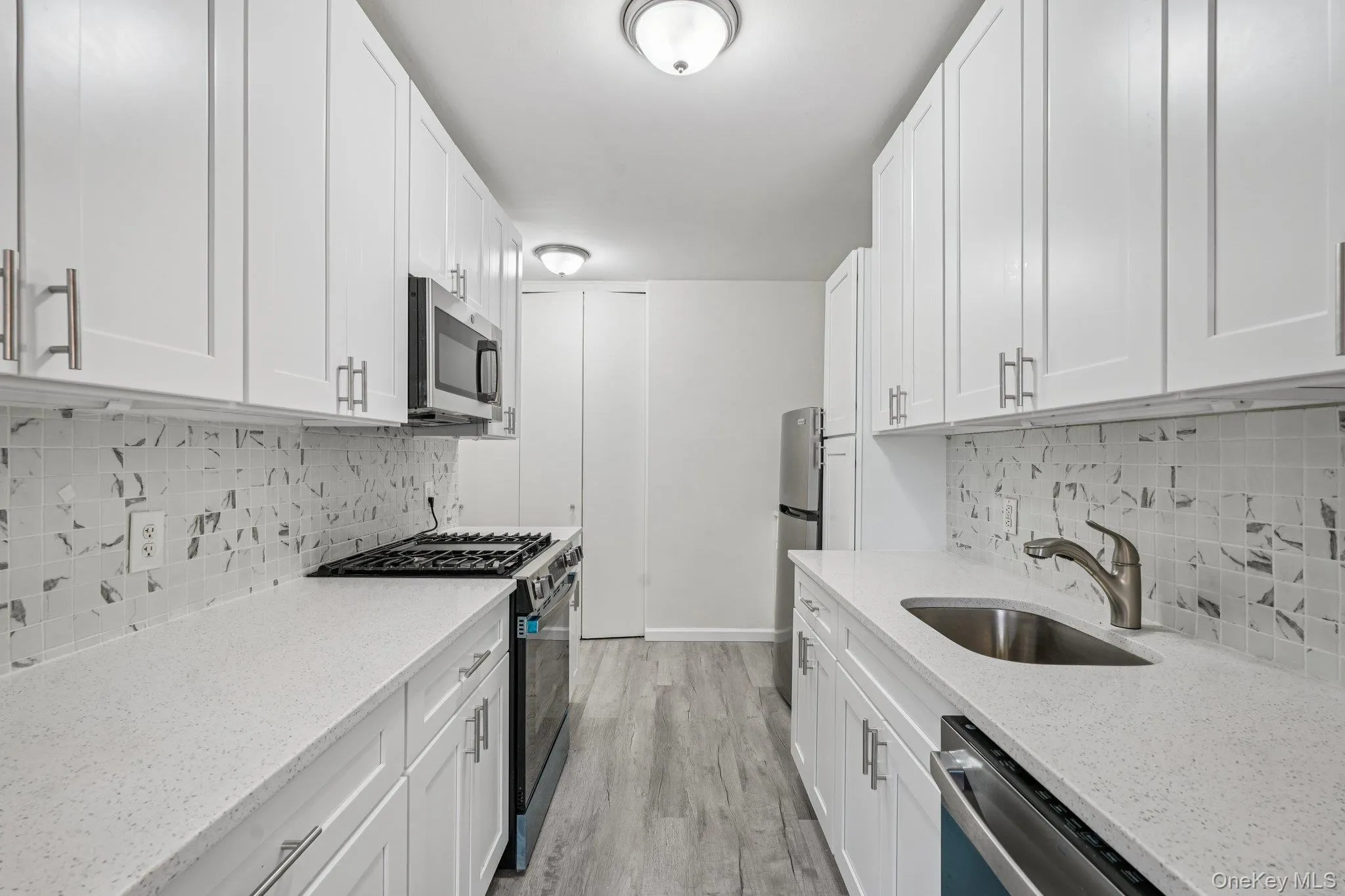 Kitchen featuring stainless steel appliances, tasteful backsplash, white cabinetry, and light stone counters Kitchen featuring stainless steel appliances, tasteful backsplash, white cabinetry, and light stone counters