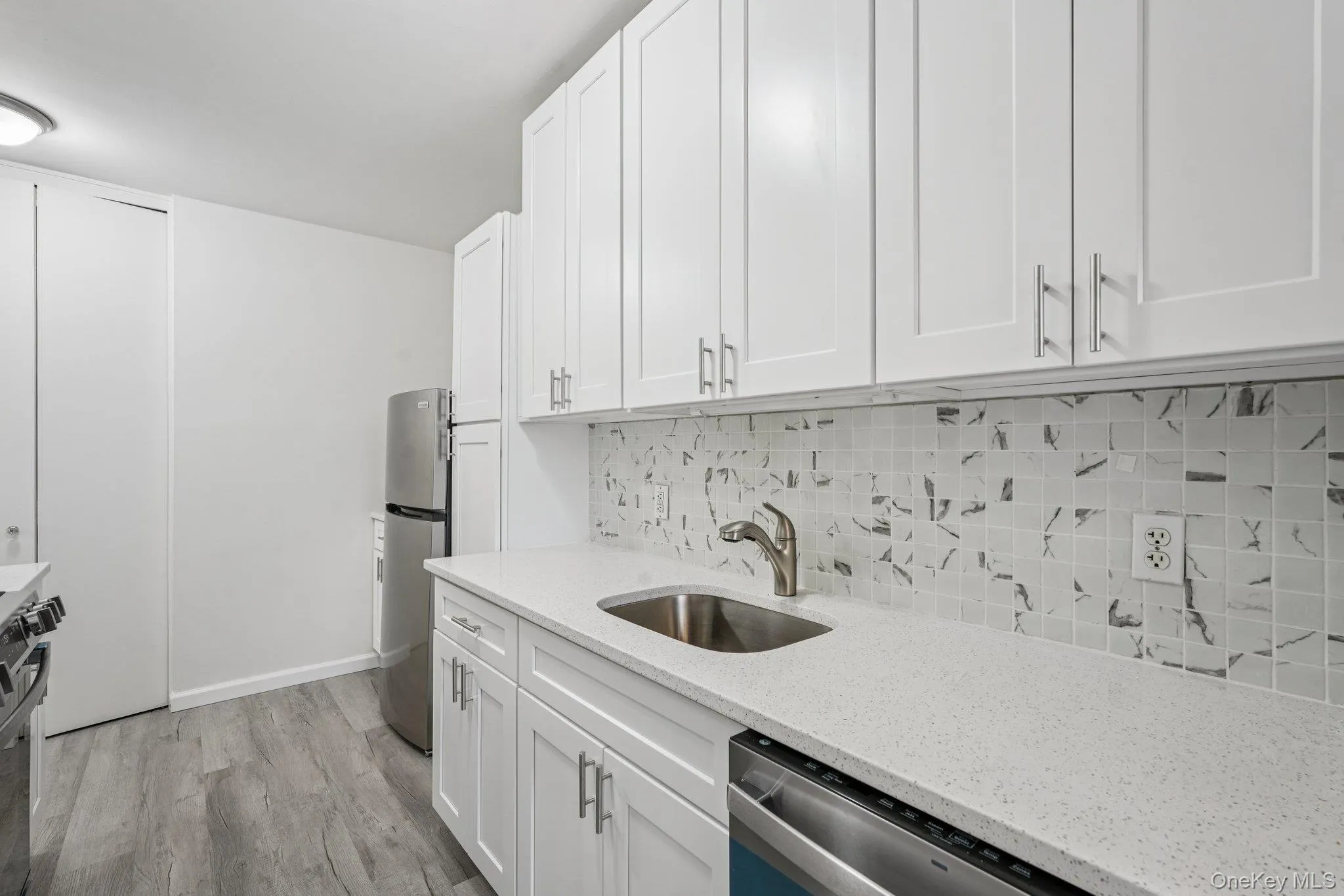 Kitchen featuring white cabinetry, light stone countertops, stainless steel appliances, light wood finished floors, and backsplash Kitchen featuring white cabinetry, light stone countertops, stainless steel appliances, light wood finished floors, and backsplash