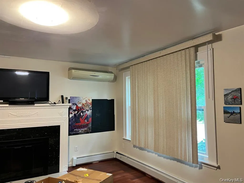 Unfurnished living room with a wall unit AC, dark wood-style floors, a glass covered fireplace, and a baseboard heating unit Unfurnished living room with a wall unit AC, dark wood-style floors, a glass covered fireplace, and a baseboard heating unit