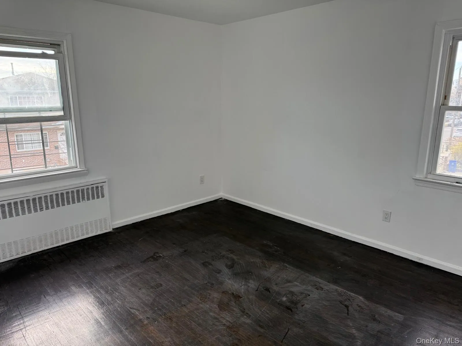 Unfurnished room featuring healthy amount of natural light, radiator, and dark wood-style floors Unfurnished room featuring healthy amount of natural light, radiator, and dark wood-style floors