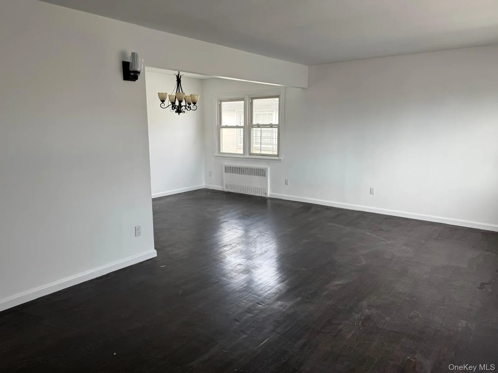 Empty room featuring radiator heating unit, a chandelier, and dark wood finished floors Empty room featuring radiator heating unit, a chandelier, and dark wood finished floors