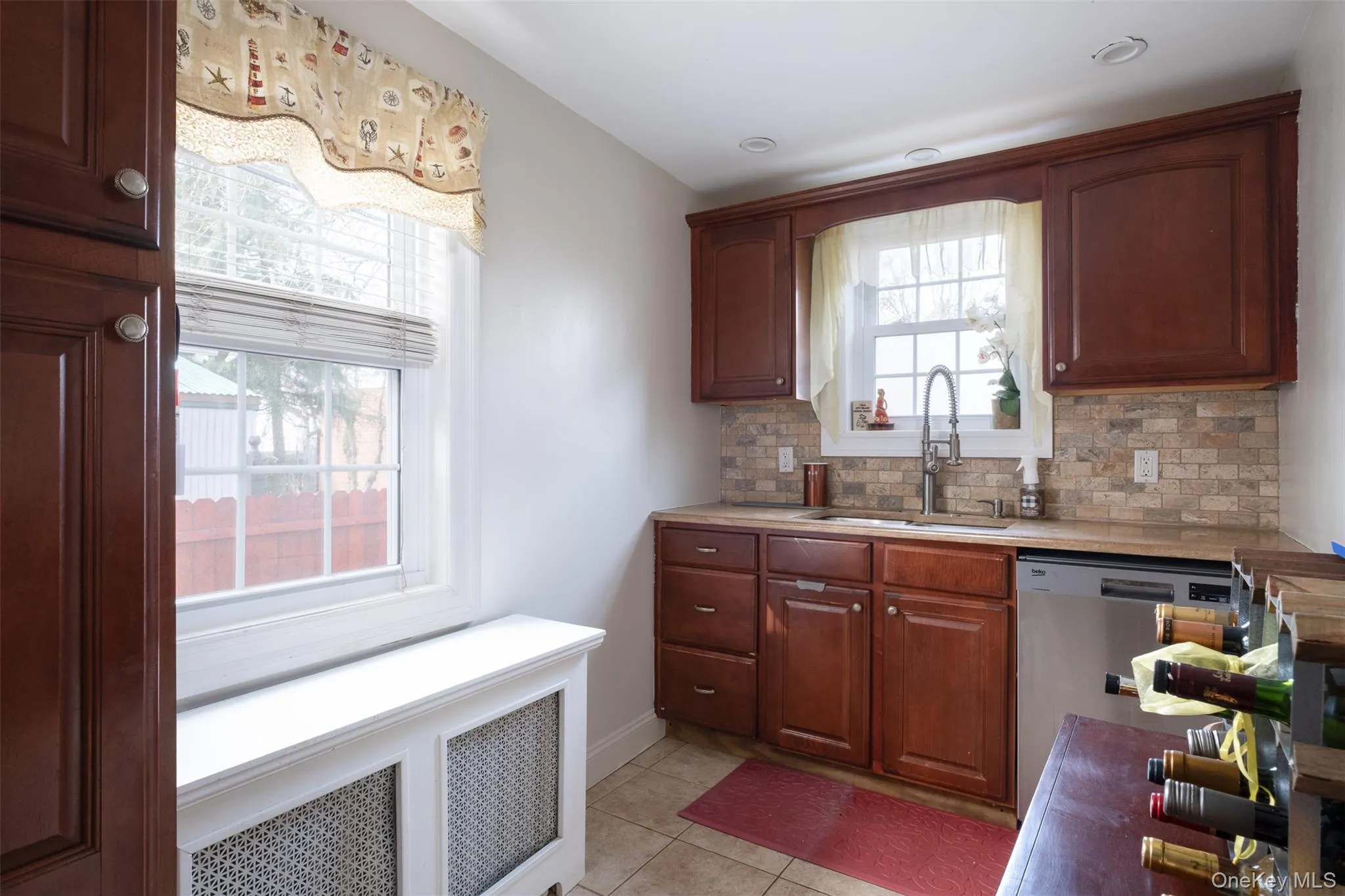 Kitchen with radiator heating unit, light countertops, decorative backsplash, stainless steel dishwasher, and light tile patterned flooring Kitchen with radiator heating unit, light countertops, decorative backsplash, stainless steel dishwasher, and light tile patterned flooring