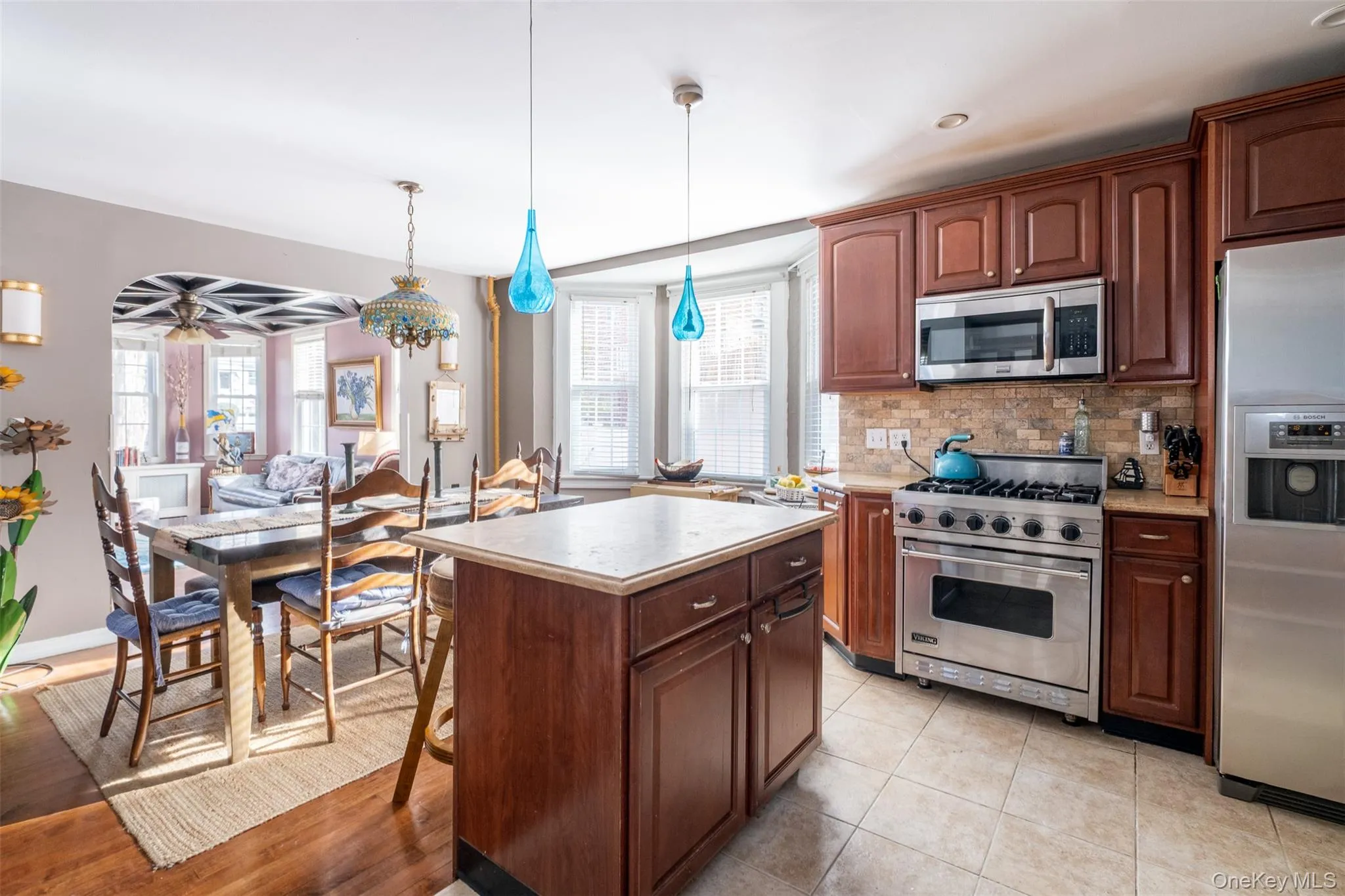 Kitchen featuring stainless steel appliances, decorative light fixtures, tasteful backsplash, light countertops, and a center island Kitchen featuring stainless steel appliances, decorative light fixtures, tasteful backsplash, light countertops, and a center island