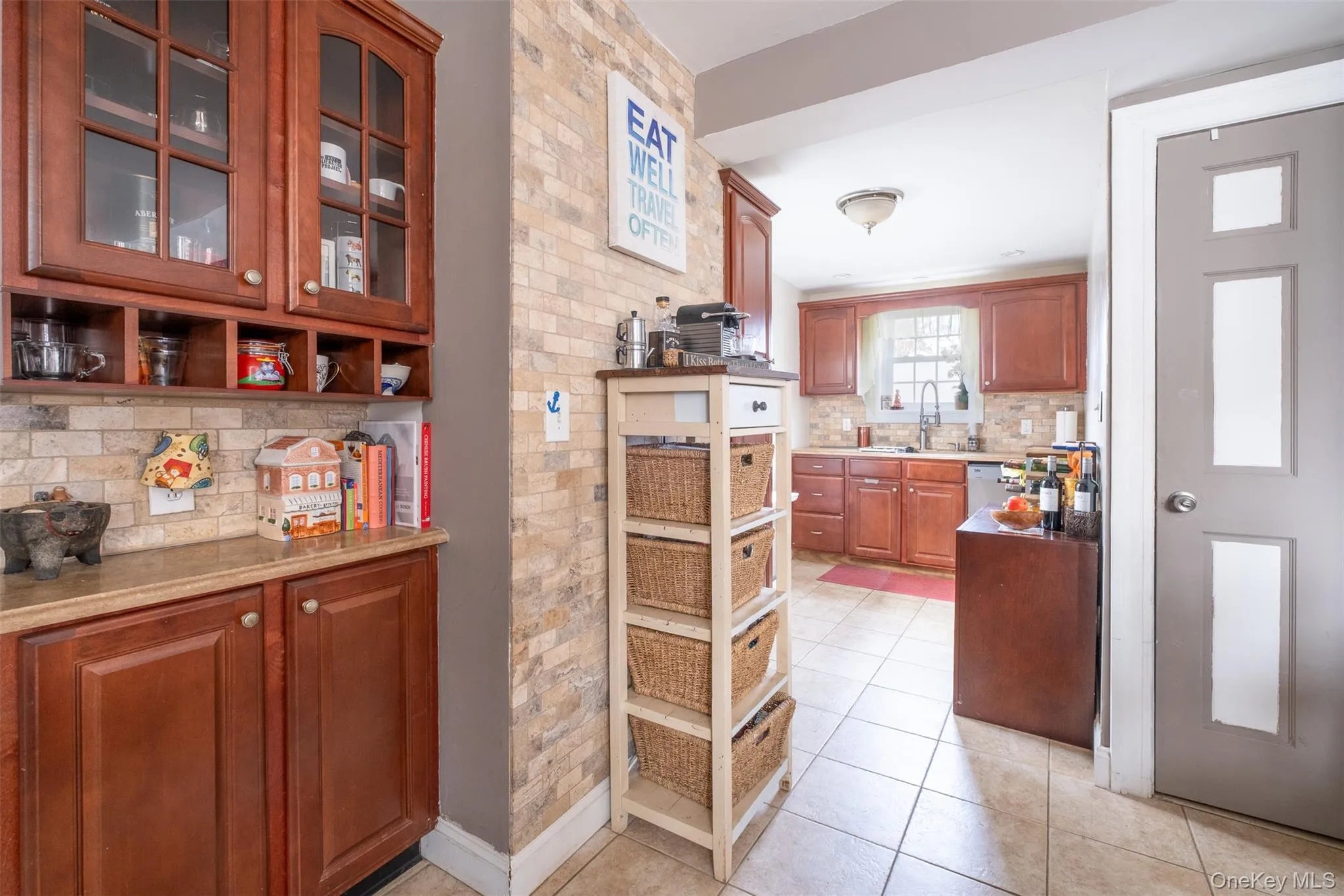 Kitchen featuring brown cabinets, decorative backsplash, light tile patterned flooring, glass insert cabinets, and light stone countertops Kitchen featuring brown cabinets, decorative backsplash, light tile patterned flooring, glass insert cabinets, and light stone countertops