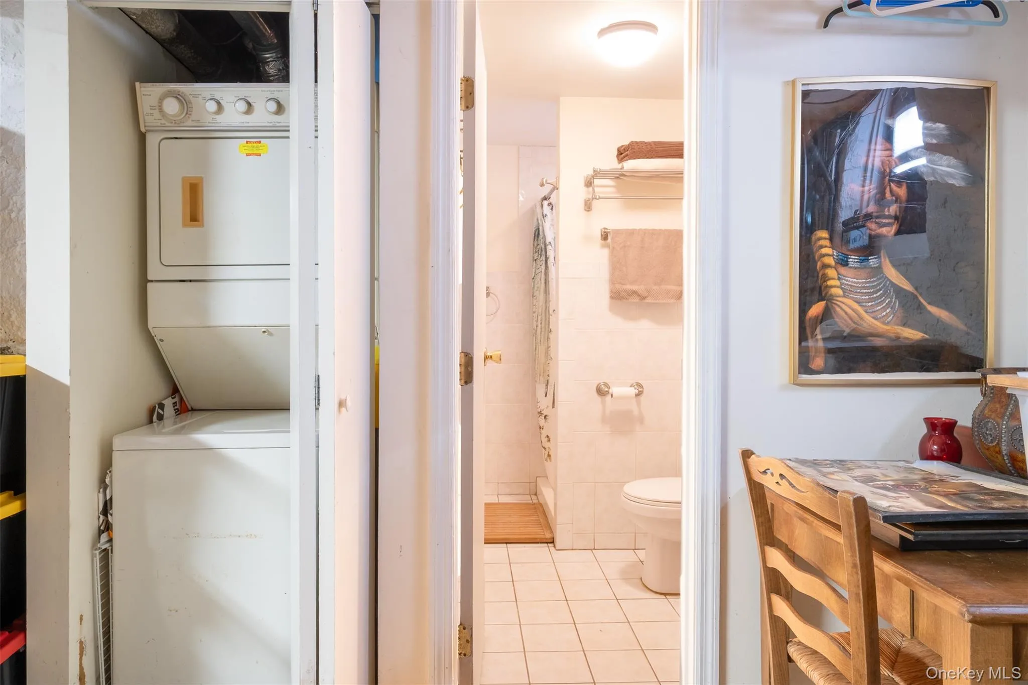 Laundry room featuring stacked washer / drying machine, tile walls, and light tile patterned floors Laundry room featuring stacked washer / drying machine, tile walls, and light tile patterned floors