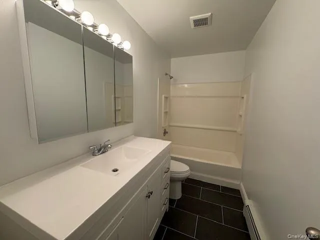 Bathroom featuring vanity, tub / shower combination, dark tile patterned ceramic tile floors, and a baseboard radiator Bathroom featuring vanity, tub / shower combination, dark tile patterned ceramic tile floors, and a baseboard radiator