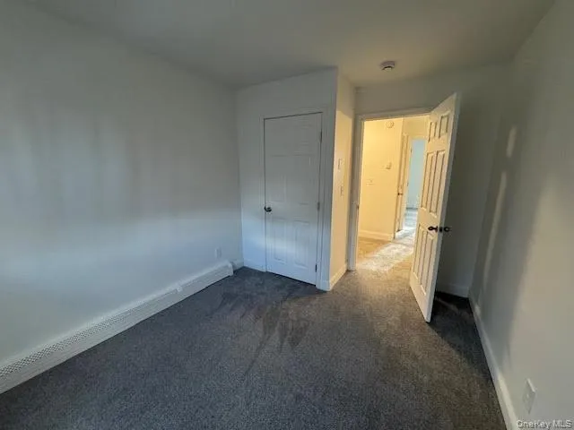 Unfurnished bedroom featuring baseboard heating, dark carpet, and a closet Unfurnished bedroom featuring baseboard heating, dark carpet, and a closet