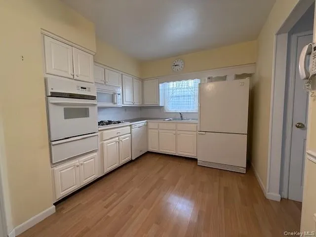 Kitchen with white appliances, white cabinets, a warming drawer, light wood-style floors, and light countertops Kitchen with white appliances, white cabinets, a warming drawer, light wood-style floors, and light countertops