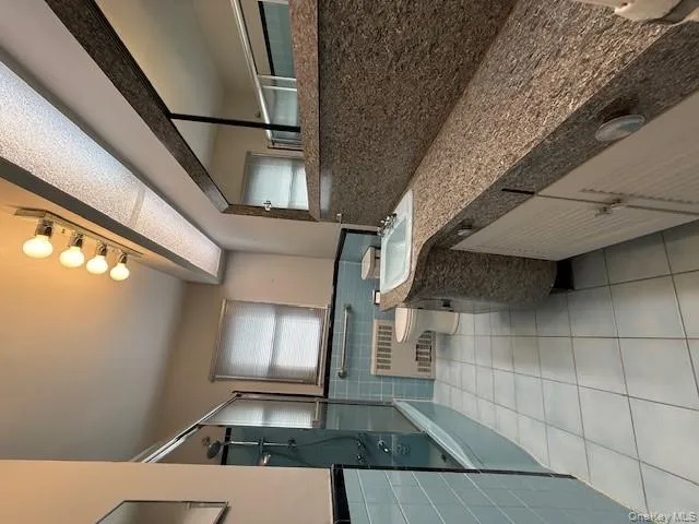 Full bath featuring light tile patterned floors, vanity, combined bath / shower with glass door, radiator, and a wainscoted wall Full bath featuring light tile patterned floors, vanity, combined bath / shower with glass door, radiator, and a wainscoted wall