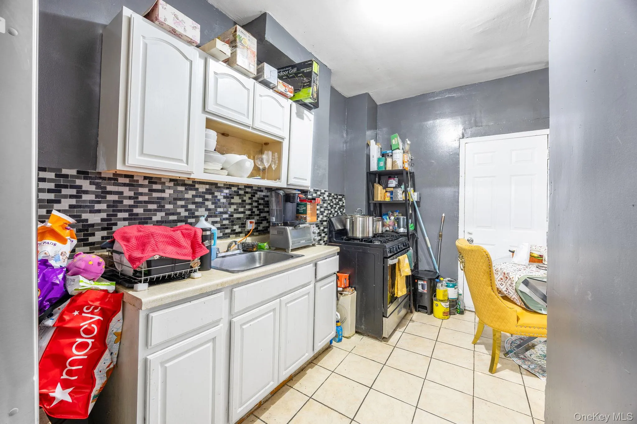 Kitchen featuring light countertops, white cabinetry, range with gas stovetop, decorative backsplash, and light tile patterned floors Kitchen featuring light countertops, white cabinetry, range with gas stovetop, decorative backsplash, and light tile patterned floors