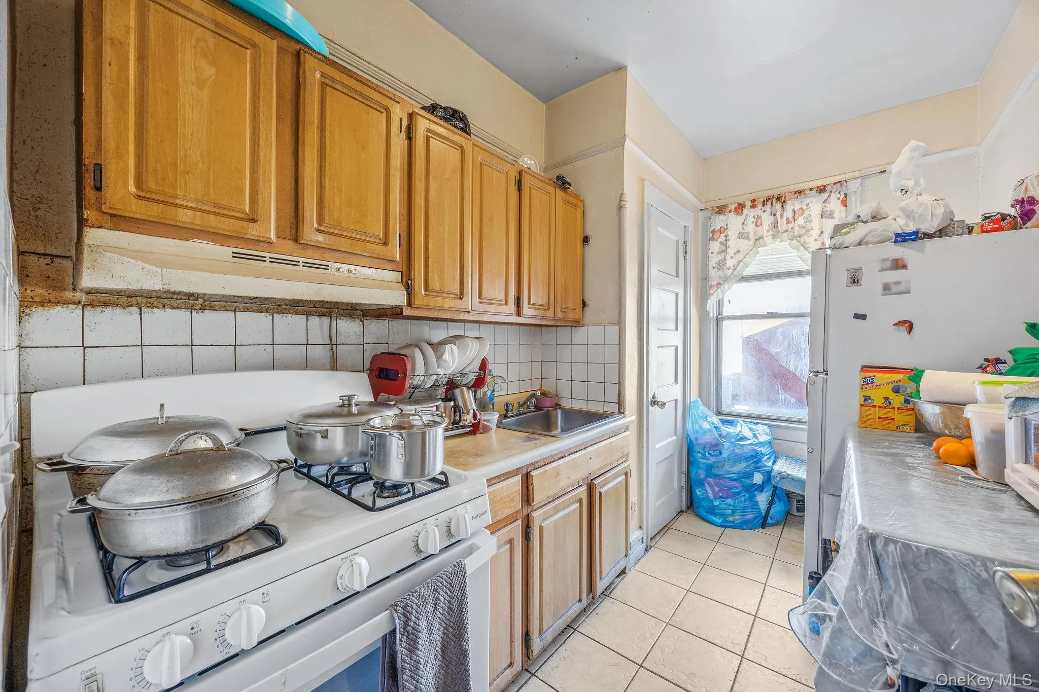 Kitchen with white appliances, light tile patterned flooring, light countertops, under cabinet range hood, and tasteful backsplash Kitchen with white appliances, light tile patterned flooring, light countertops, under cabinet range hood, and tasteful backsplash