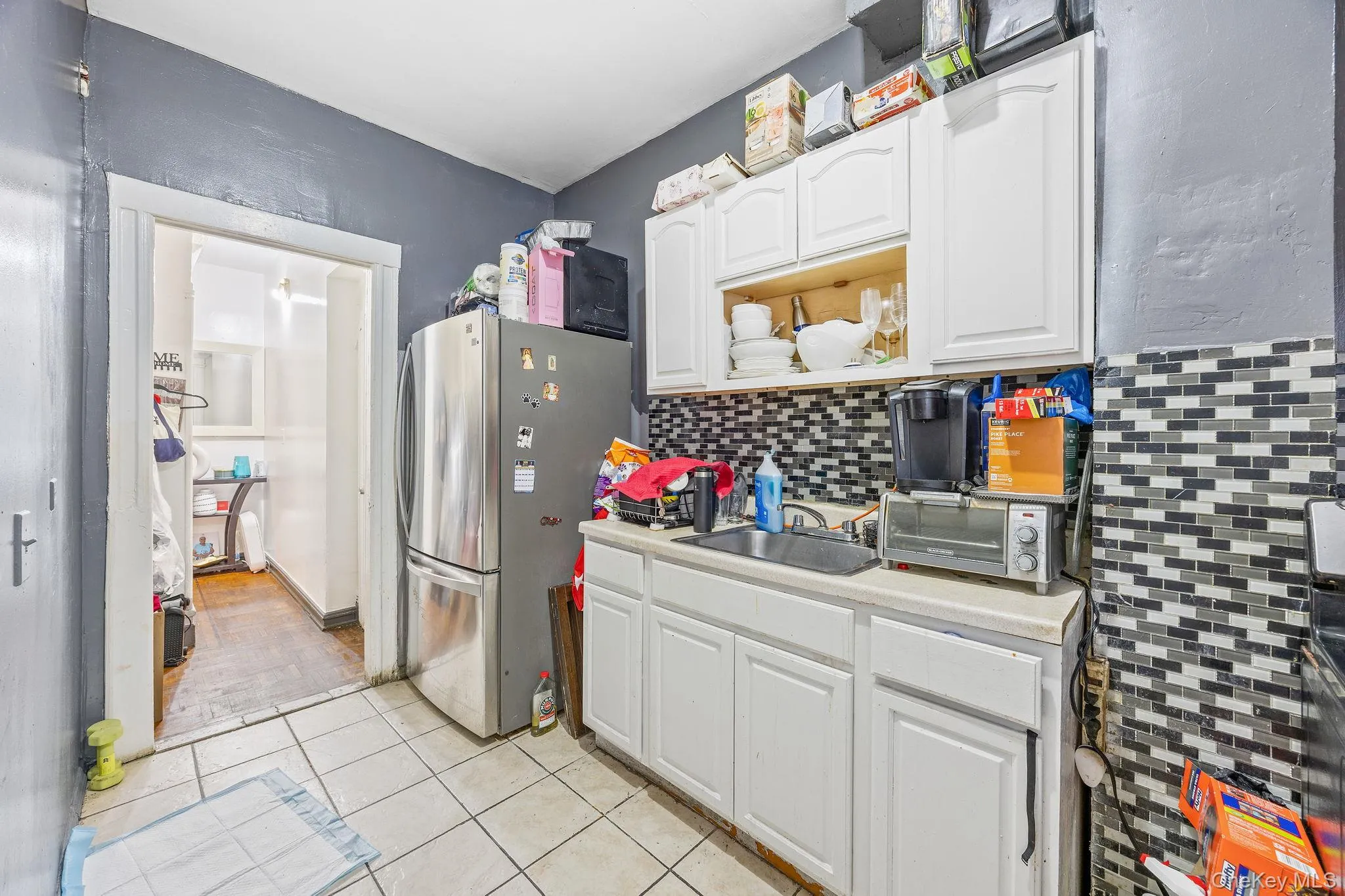 Kitchen with white cabinets, freestanding refrigerator, light countertops, light tile patterned floors, and backsplash Kitchen with white cabinets, freestanding refrigerator, light countertops, light tile patterned floors, and backsplash