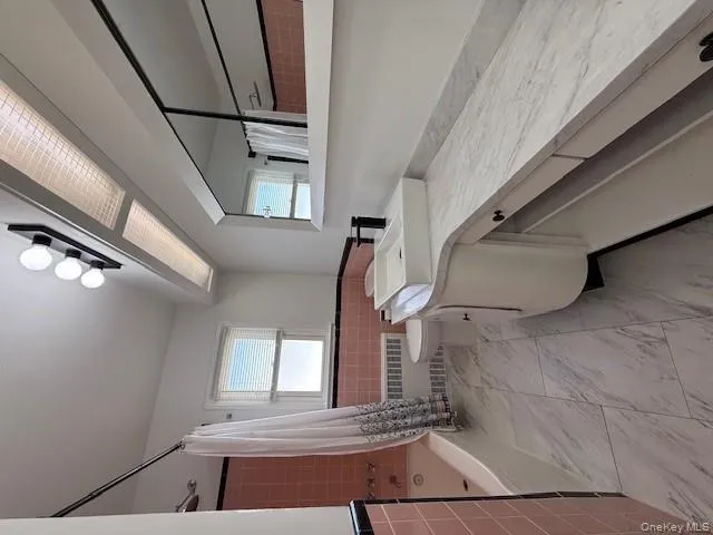 Bathroom with a wainscoted wall, tile walls, vanity, radiator, and shower / bathtub combination with curtain Bathroom with a wainscoted wall, tile walls, vanity, radiator, and shower / bathtub combination with curtain