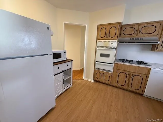 Kitchen featuring white appliances, brown cabinetry, light wood-style floors, and a warming drawer Kitchen featuring white appliances, brown cabinetry, light wood-style floors, and a warming drawer