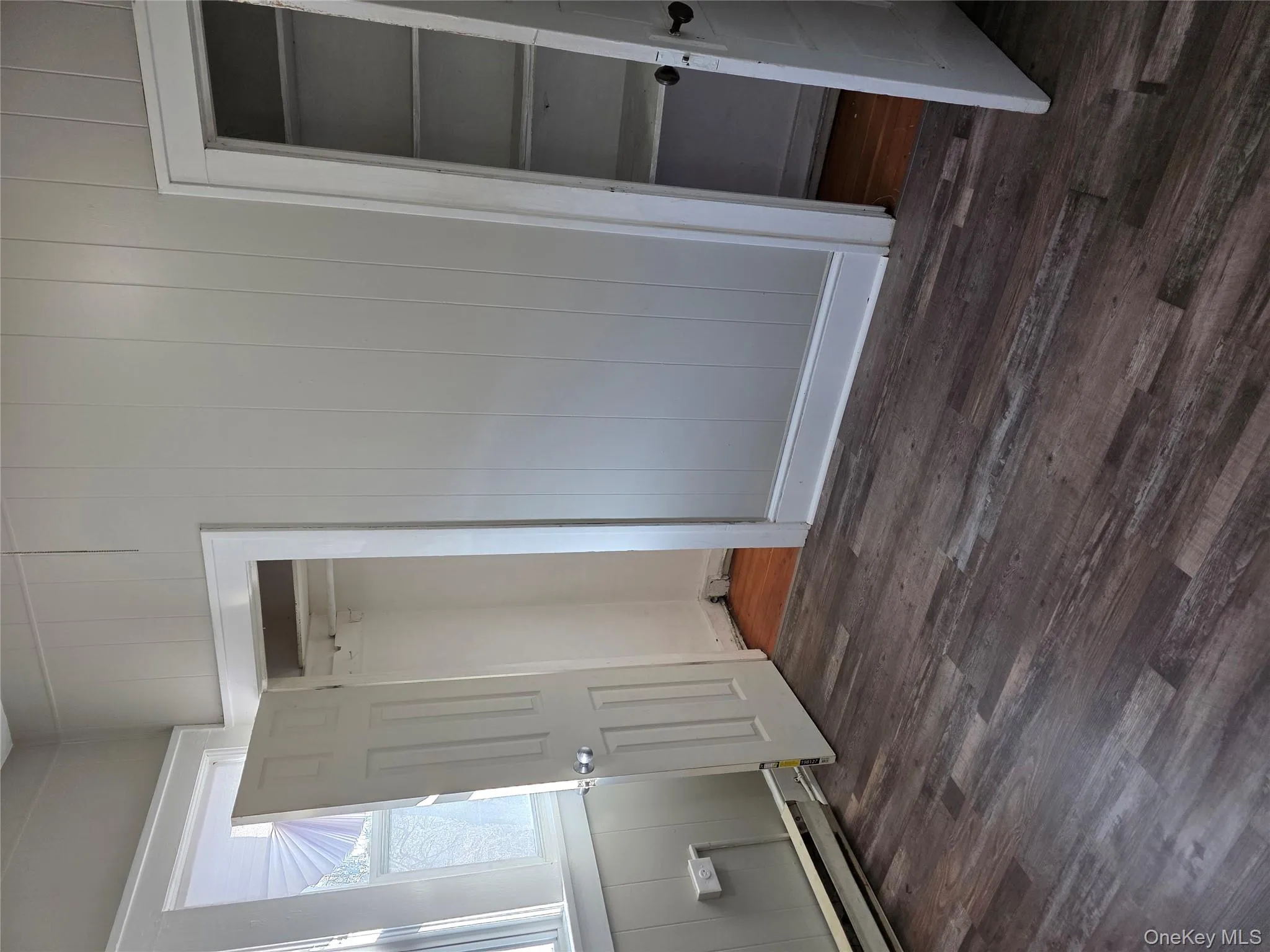 Unfurnished bedroom featuring dark wood-style floors, wooden walls, and a baseboard radiator Unfurnished bedroom featuring dark wood-style floors, wooden walls, and a baseboard radiator