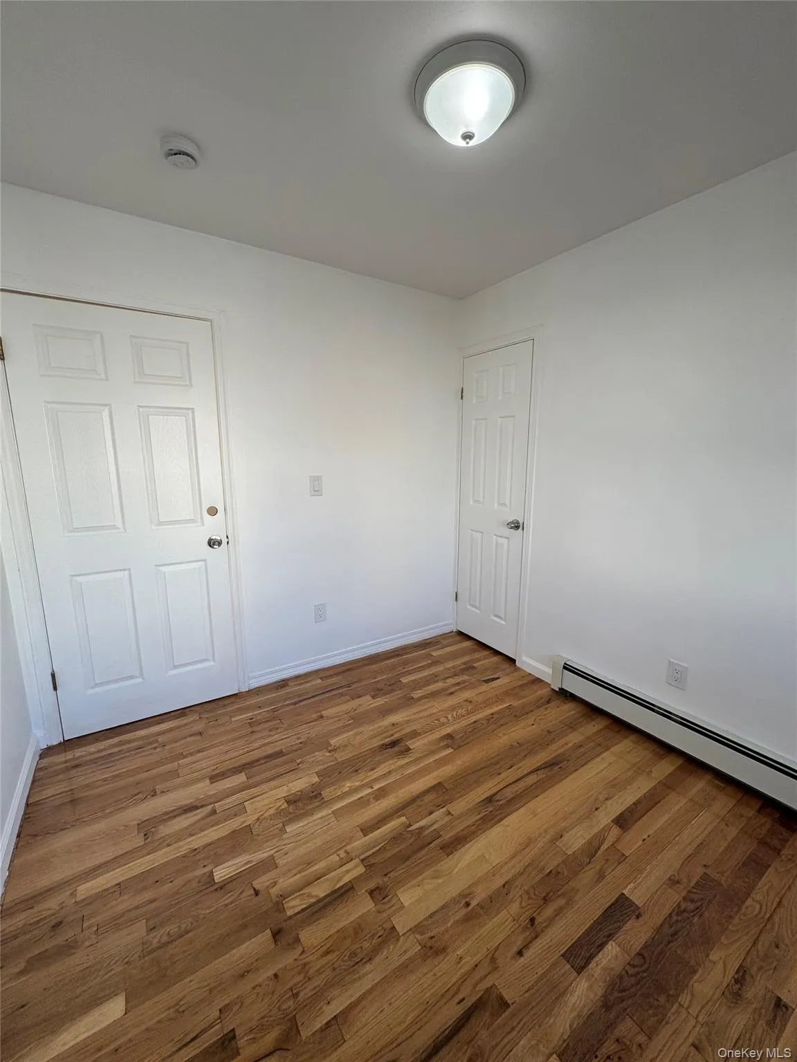Unfurnished room with a baseboard heating unit and wood finished floors Unfurnished room with a baseboard heating unit and wood finished floors