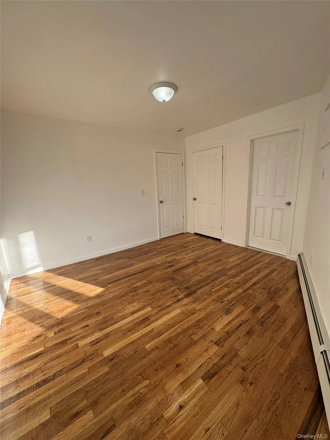 Unfurnished bedroom with wood-type flooring and baseboard heating Unfurnished bedroom with wood-type flooring and baseboard heating