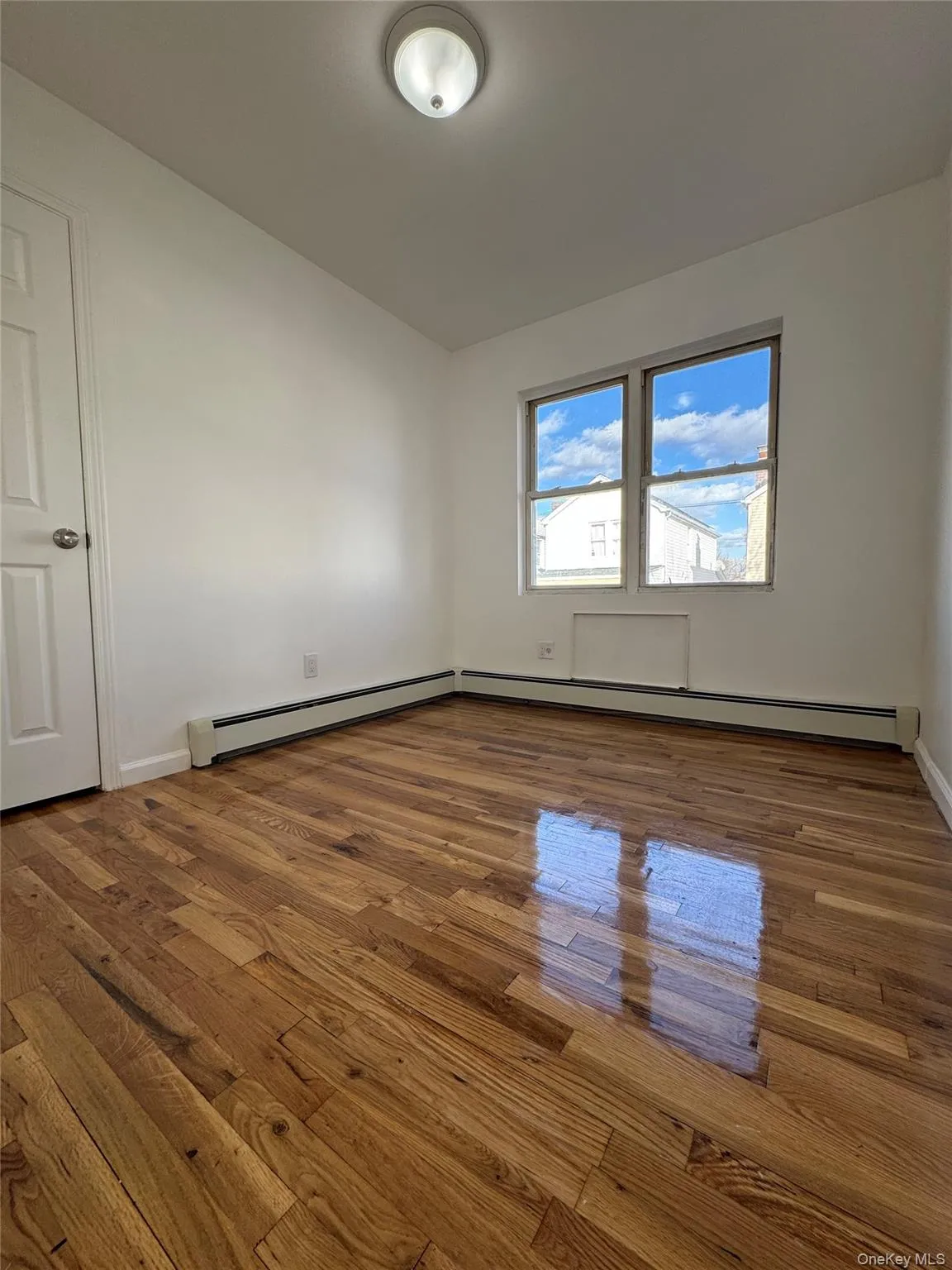 Empty room with dark wood-style flooring and a baseboard heating unit Empty room with dark wood-style flooring and a baseboard heating unit