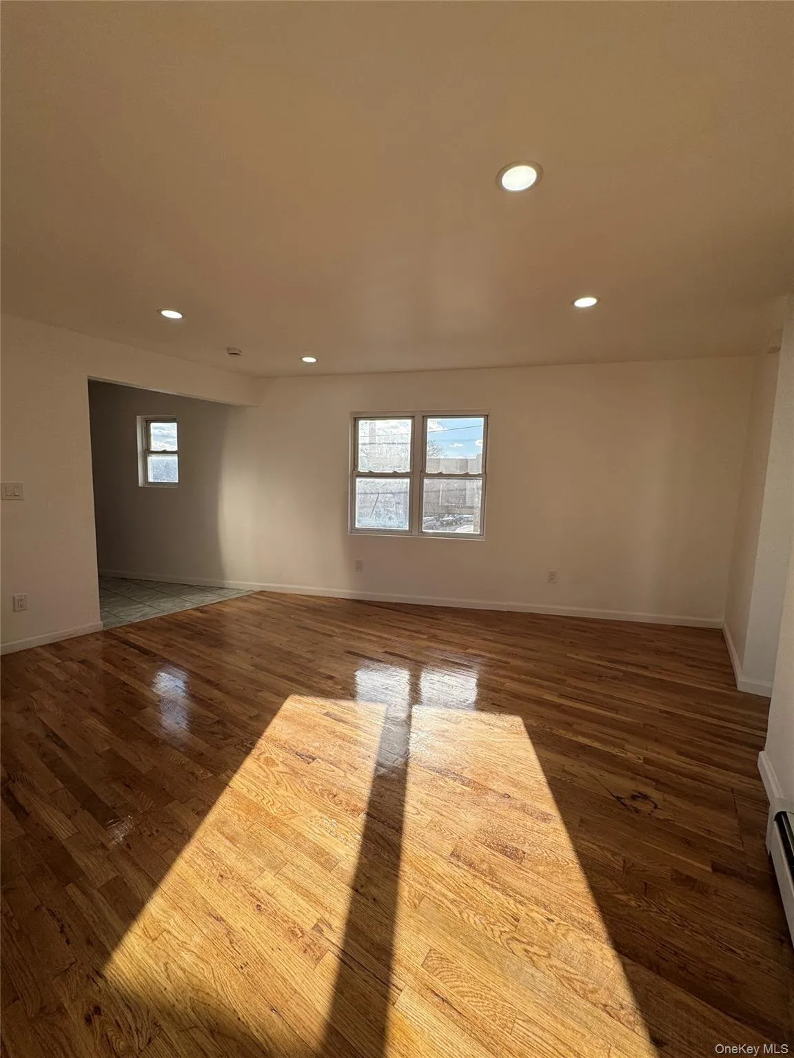 Empty room with recessed lighting, dark wood-style flooring, and a baseboard heating unit Empty room with recessed lighting, dark wood-style flooring, and a baseboard heating unit