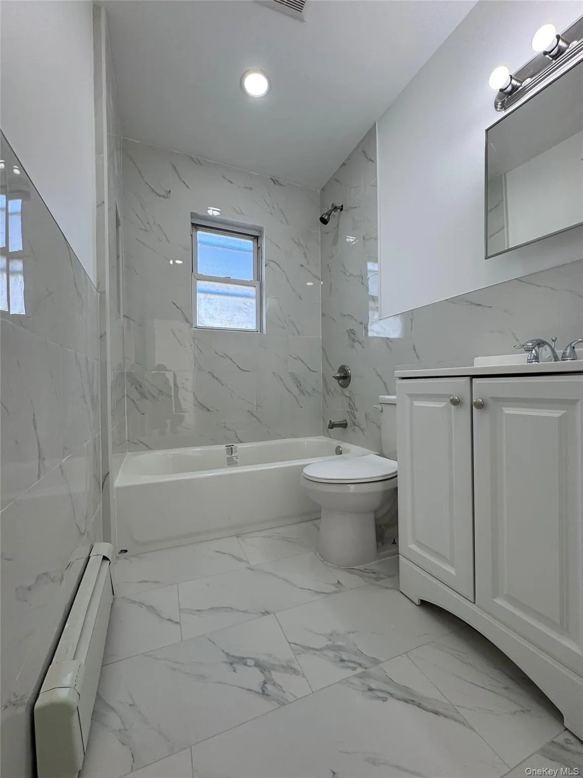Bathroom featuring vanity, a baseboard heating unit, a combined bath / shower with marble appearance, light marble finish flooring, and recessed lighting Bathroom featuring vanity, a baseboard heating unit, a combined bath / shower with marble appearance, light marble finish flooring, and recessed lighting