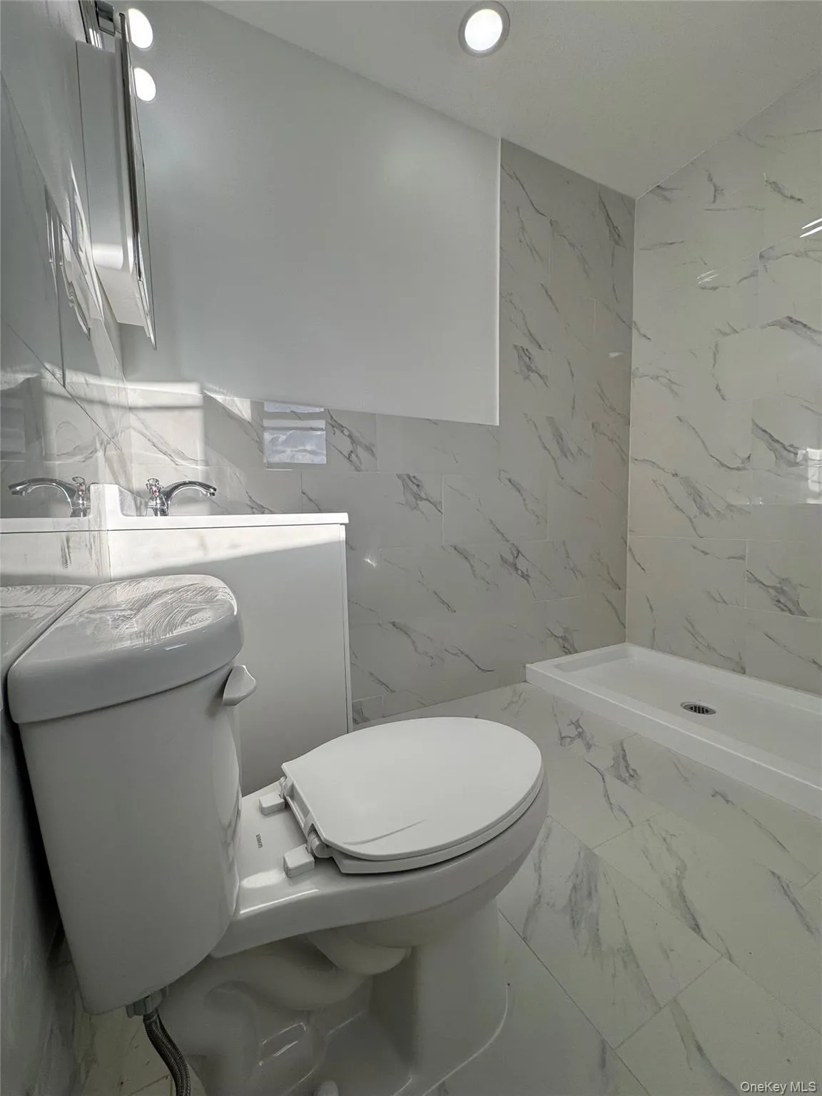 Full bath with marble tiled flooring, a marble finish shower, stone wall, tile walls, and recessed lighting Full bath with marble tiled flooring, a marble finish shower, stone wall, tile walls, and recessed lighting