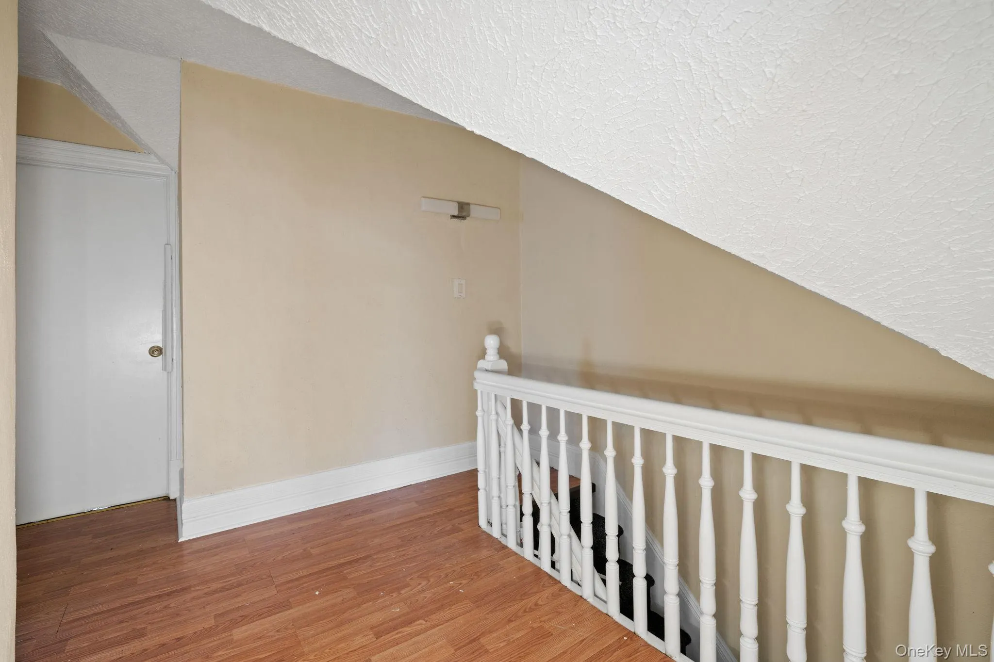 Hallway featuring wood finished floors, lofted ceiling, and a textured ceiling Hallway featuring wood finished floors, lofted ceiling, and a textured ceiling