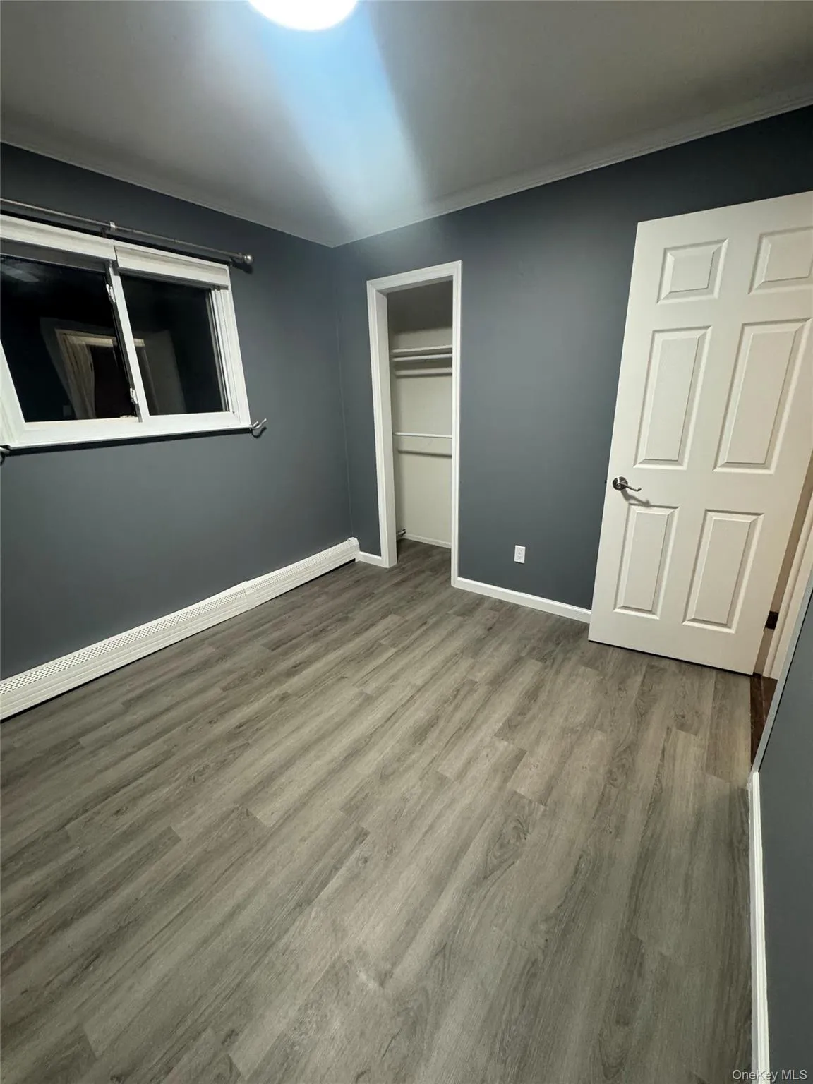 Unfurnished bedroom featuring a baseboard heating unit, wood finished floors, and a closet Unfurnished bedroom featuring a baseboard heating unit, wood finished floors, and a closet