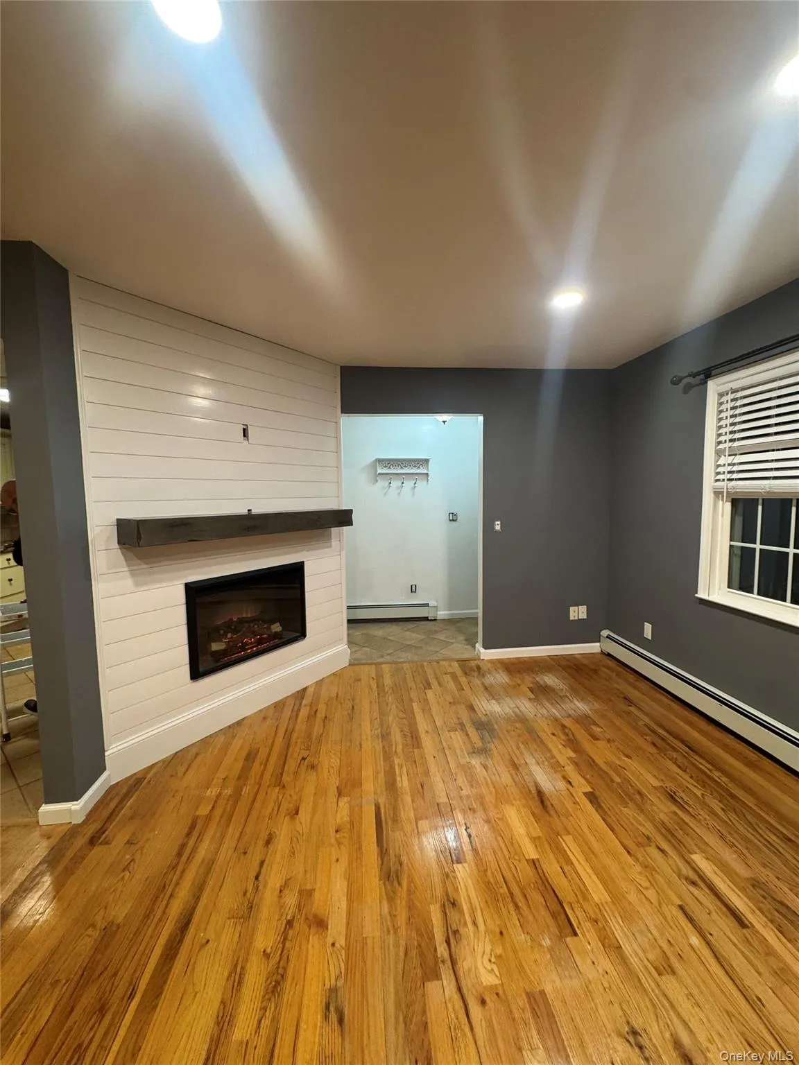 Unfurnished living room featuring baseboard heating, light wood finished floors, and a fireplace Unfurnished living room featuring baseboard heating, light wood finished floors, and a fireplace